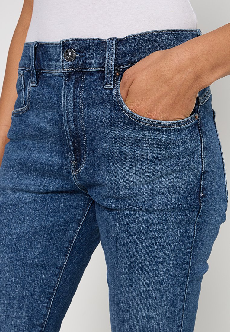 Jeans en denim bleu foncé avec un design classique à cinq poches, une texture légèrement délavée et une fermeture à bouton visible sur le devant.