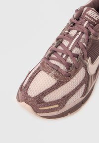 Πάφος Nike Vomero σε σκούρο μοβ και ανοιχτό ροζ. Διαθέτει αναπνεύσιμο δίχτυ, υφασμάτινες λεπτομέρειες και μαξιλαρωμένη γλώσσα με λογότυπο.