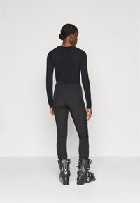 Crna majica dugih rukava, prilagođenog dizajna, uparena s crnim skijaškim hlačama i crnim skijaškim čizmama. Glatka tekstura, minimalni detalji i elegantna silueta.