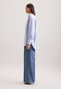 Camicia a righe blu con maniche lunghe, abbinata a una lunga gonna di denim. Il tessuto è leggero; il design è di taglio rilassato.