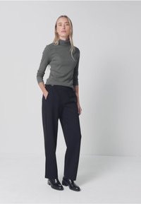 Grå polotröja, svarta högmidjade byxor och svarta ankelstövlar. Mjuk tyg och avslappnad passform med sidfickor. Slät textur.