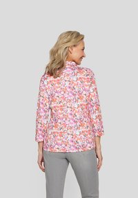 Damenbluse mit langen Ärmeln im pinken und orangefarbenen Blumenmuster, mit einem Stehkragen und einem lockeren Schnitt. Weicher, leichter Stoff.