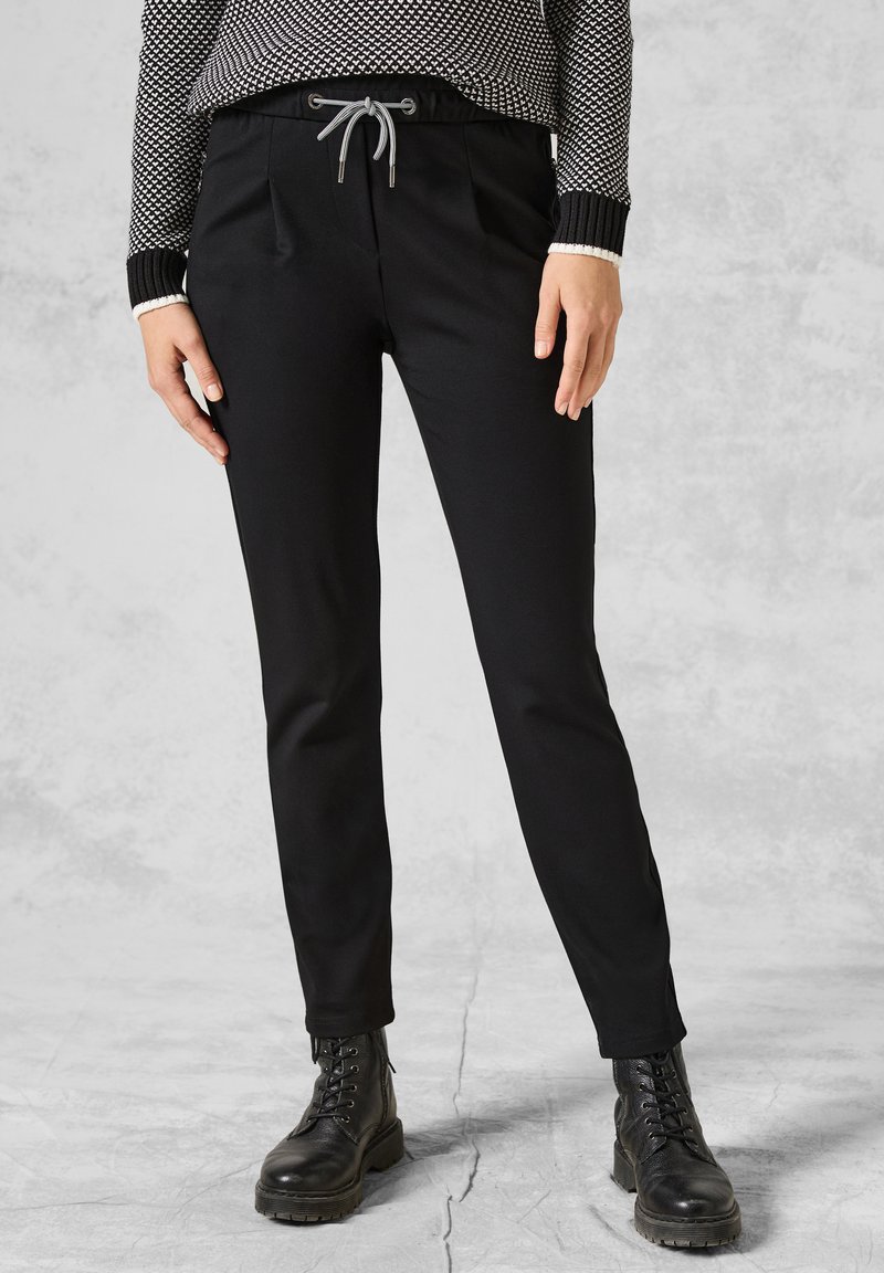 Svarta tapered byxor med elastisk midja och dragsko, med två sidfickor och en mjuk tygstruktur, kombinerade med svarta kängor.
