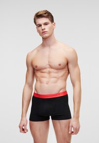 Boxers noirs avec une ceinture rouge portant le texte "KARL LAGERFELD". Tissu lisse, design ajusté et longueur mi-cuisse.