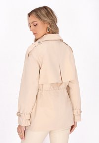 Trench coat beige con vita stretta, polsini con cintura e dettaglio di apertura posteriore, realizzato in un tessuto leggero.
