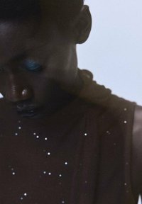 Îmbrăcăminte de culoare brown cu o suprafață texturată, împodobită cu mici paiete argintii, evidențiind un design lejer. Fardul de pleoape albastru completează aspectul.