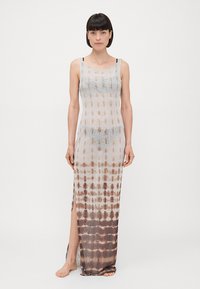 Long, sheer dress with a tie-dye pattern in brown and beige. Features thin straps and a side slit for added movement. Lightweight fabric.