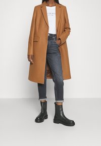 Bruin wollen blend jas met een aangesloten ontwerp, witte graphic t-shirt en marineblauwe jeans. Zwarte enkelboots met een robuuste zool.