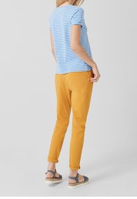 Sinisen ja valkoisen raidallinen t-paita, keltaiset housut ja harmaat sandaalit. Housut on käännetty lahkeista; sileä kankaan rakenne.