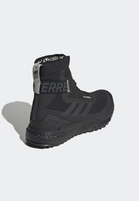 Botte de sport montante noire avec semelle épaisse, dessus en tissu, bride de marque et languette au talon sur un fond clair uni.