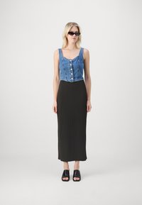 Denim crop top nööpidega ees, koos ribakujulise musta maxi-seelikuga ja mustade avatud varvastega sussidega. Mudel kannab kassisilma päikeseprille.