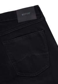 Un bolsillo trasero de unos vaqueros de mezclilla negra con costuras visibles y una etiqueta de marca de cuero negro que dice "MUSTANG" en la cintura.