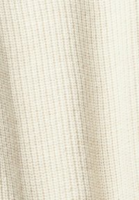 Wollpulloverstoff mit geripptem Muster in Cremefarbe, der ein weiches, gestricktes Design mit unterschiedlicher Dicke aufweist.