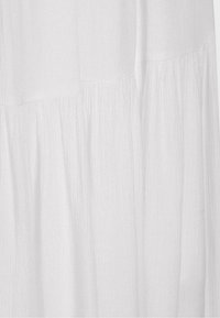 Weißer, leichter Stoff mit subtiler Textur und gerafften Nähten, die sanfte vertikale Falten und ein fließendes Aussehen erzeugen.