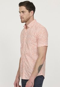 Korte mouwen shirt in lichtoranje met een klein wit bloemenpatroon, met knoopsluiting en een slim fit ontwerp. Zacht materiaal met een gladde textuur.