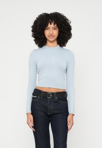 Ανοιχτό μπλε ριμπ μακρυμάνικο crop top με στρογγυλή λαιμόκοψη, συνδυασμένο με σκούρες τζιν παντελόνες και μαύρη ζώνη, αποκαλύπτοντας καθορισμένη υφή και εφαρμογή.