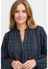 Blusa a maniche lunghe, blu scuro con motivo, caratterizzata da un colletto a V, polsini elasticizzati e intricati disegni geometrici neri.