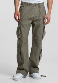 Pantaloni cargo din bumbac verde oliv, cu multiple buzunare laterale și o croiala relaxată. Prezintă o închidere cu buton și o betelie ajustabilă. Poartă adidași albi.