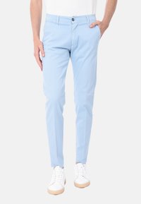 Chino in cotone blu chiaro con vestibilità slim e design a vita alta. Presenta tasche frontali e chiusura a bottone in vita, abbinati a sneaker bianche.