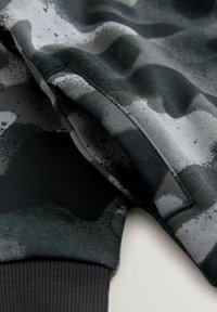 Szürke és fekete árnyalatú, terepmintás szövet, amely puha tapintású, ribbelt szegéllyel és látható varrásokkal rendelkezik.