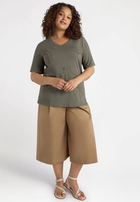 Top verde oliva con escote en V y mangas cortas, adornado con diseños de cuentas, combinado con pantalones de pierna ancha color beige y sandalias ligeras con tiras.