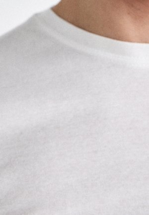 White cotton T-shirt with a crew neckline, featuring a smooth texture and minimal stitching detail. Close-up view of the neckline.