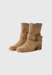 Bottines en suede beige avec un bout rond, une fermeture éclair sur le côté, une large sangle avec une boucle en métal et un talon en bois épais.