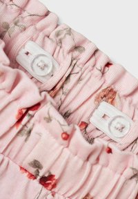 Tessuto floreale rosa con bordi arricciati, dotato di fasce elastiche bianche e bottoni. Il design include piccoli motivi di fiori rossi e verdi.