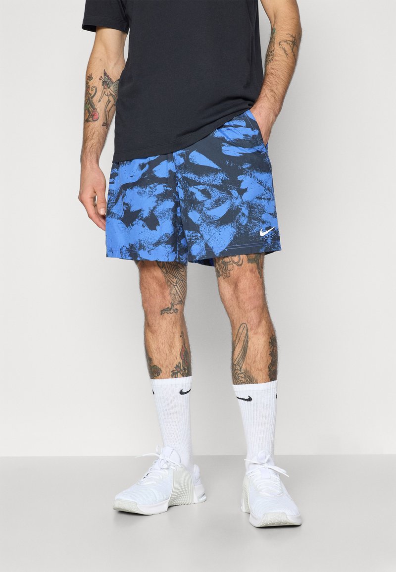 I pantaloni da bagno a fantasia blu presentano un design astratto blu e nero. Indossati con calze sportive bianche e sneakers, mostrano un look informale.