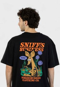 Musta t-paita, jossa on suuri graafinen kuva takana tekstillä "SNIFF'S BUSINESS" ja piirros sarjakuvahahmosta, jolla on laukut.