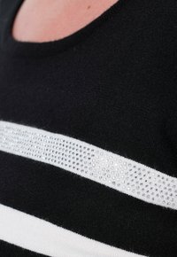 Czarny i biały sweter w paski z dekoltem w serek, z wyraźnym poziomym pasem przejrzystych cyrkonii na klatce piersiowej.