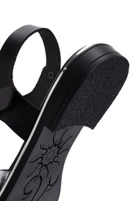Sandalo nero con suola in gomma testurizzata, cinturini lisci e un motivo decorativo a forma di sole sulla soletta. Cinturino posteriore regolabile per una vestibilità ottimale.