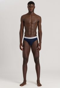 Slip blu navy da uomo con elastico bianco riportante il logo "HANRO" in rilievo. Il materiale sembra elastico e morbido, garantendo una vestibilità aderente.
