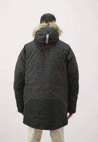 Sort parka-jakke med pelsforet hætte, med en mat overflade, tætsiddende manchetter og lynlås; designet til koldt vejr.