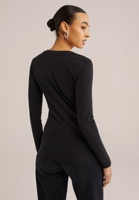 Juodos medvilnės ilgomis rankovėmis marškiniai su apvaliu kaklu ir lygiu paviršiumi, pasižymintys prigludusia forma ir šiek tiek išlenktu apvadu.