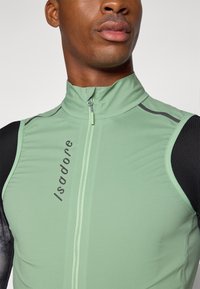 Grüne Radweste mit hohem Kragen und Frontreißverschluss. Mit schwarzen Akzenten und dem Text "Isadore" auf der Vorderseite. Glattes, körpernahes Material.