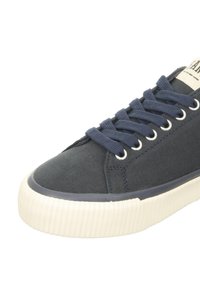 Navy canvas sneaker with round toe, white rubber sole, and navy laces. Features metal eyelets and textured fabric finish.