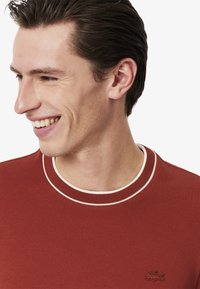 Felpa rossa con texture, con profilo bianco a coste sul collo. Presenta un piccolo logo ricamato sul petto.
