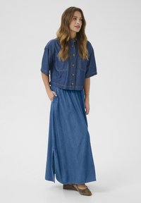 Denim cropped jakke med korte ærmer og knaplukning, parret med en lang denimnederdel med sideslids, begge i en mellemblå nuance.