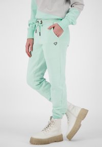 Mintgröna mjukisbyxor med dragsko i midjan, sidofickor och en liten hjärtlogo. Matchas med kraftiga vita stövlar. Mjuk bomullstyg.