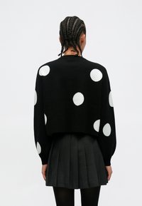 Camisola preta curta com grandes bolinhas brancas. Tecido de malha com mangas compridas e punhos canelados. Combinada com uma saia preta plissada.