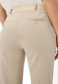 BeigeTailored-Hosen mit einer dezent strukturierten Oberfläche, ausgestattet mit einem glatten Gürtel, zwei Gesäßtaschen und einem Knopfdetail.