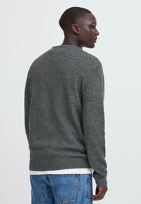 Grauer Strickpullover mit Rundhalsausschnitt, gerippten Bündchen und Saum. Über einem weißen Shirt getragen, hat er eine lockere Passform und eine glatte Textur.
