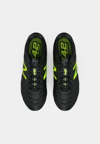 Černé fotbalové boty s prošívanou texturou, s neonově zelenými akcenty a brandingem, a černými tkaničkami. Gumová podrážka pro lepší přilnavost.