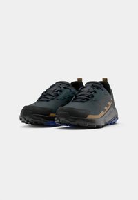 Svarta och teal trail-skor har en texturerad ovandel, bruna accenter och en robust sula med blå detaljer, utformade för prestanda och hållbarhet.