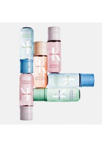 Collection de parfums corporels Calvin Klein dans des bouteilles semi-transparentes. Les couleurs incluent bleu clair, pêche, rose et vert, avec des accents métalliques.