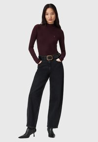 Burgunderfarbener Langarm-Top mit Stehkragen, kombiniert mit hochtaillierten schwarzen, weiten Jeans und schwarzen spitzen Stiefeletten. Großes Gurtelschnalle-Detail.