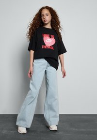 Zwarte oversized t-shirt met rode grafische tekst "LOVE TO AIR THE MAX" gecombineerd met lichtblauwe wijde jeans en beige sneakers.