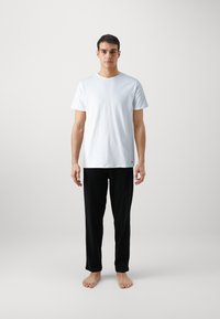 T-shirt en coton blanc à manches courtes, col rond ; associé à un pantalon noir léger à jambes droites. Pas de motifs ou accents visibles.