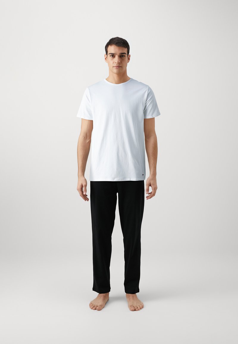 T-shirt en coton blanc à manches courtes, col rond ; associé à un pantalon noir léger à jambes droites. Pas de motifs ou accents visibles.